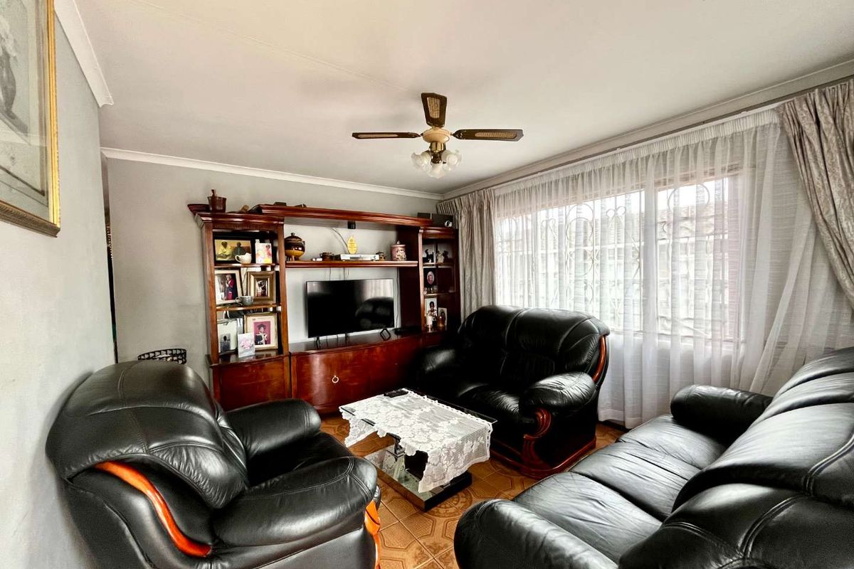 A living room featuring tiled flooring, a ceiling fan, and a large window with security bars.