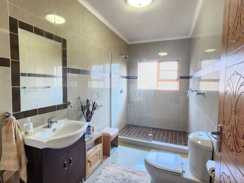 A well-maintained bathroom featuring a modern vanity, walk-in shower with glass screen, and neutral wall tiling.
