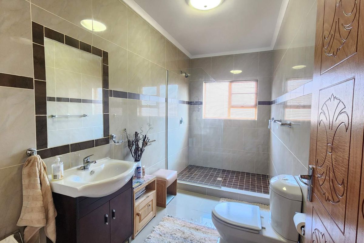 A well-maintained bathroom featuring a modern vanity, walk-in shower with glass screen, and neutral wall tiling.