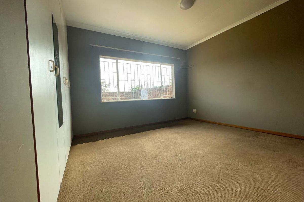 An empty bedroom featuring built-in cupboards, carpeted flooring, and security bars on the window, offering a blank canvas for potential updates.