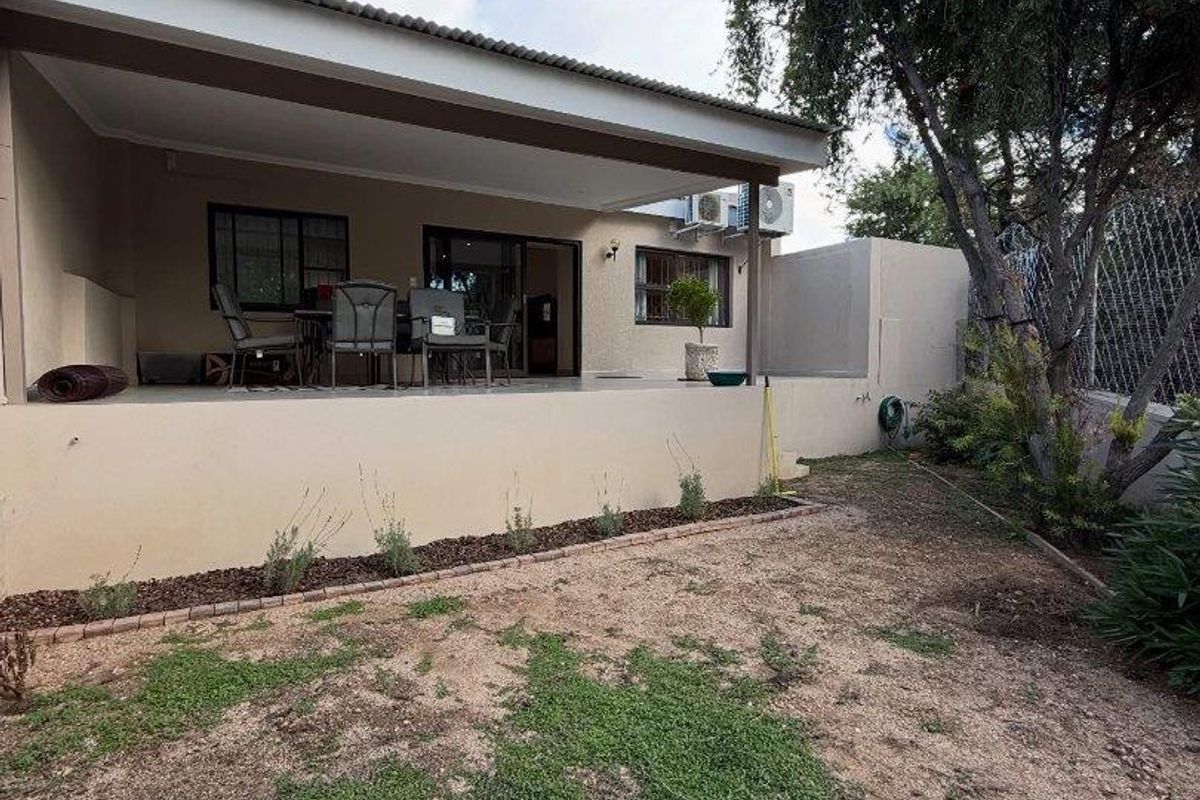 A covered rear patio area overlooking a garden space with established trees and perimeter fencing.