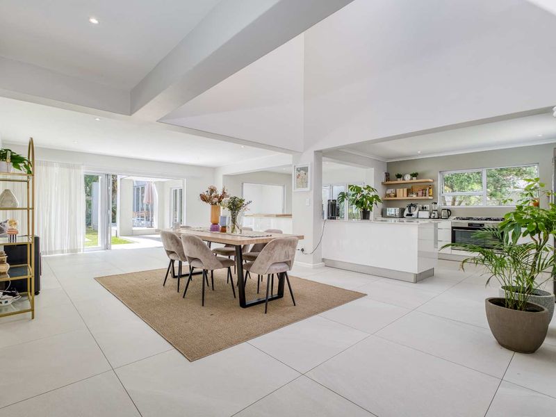Spacious open-plan living and dining area featuring high vaulted ceilings, modern tiled flooring, and a sleek kitchen with integrated appliances and direct patio access.