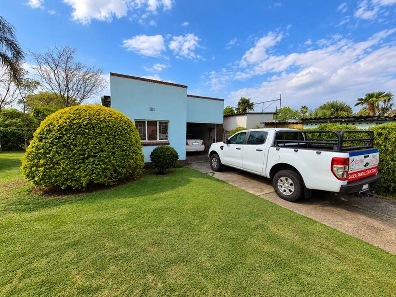 Front elevation of a single-story house featuring a concrete driveway, attached garage, and established garden area.