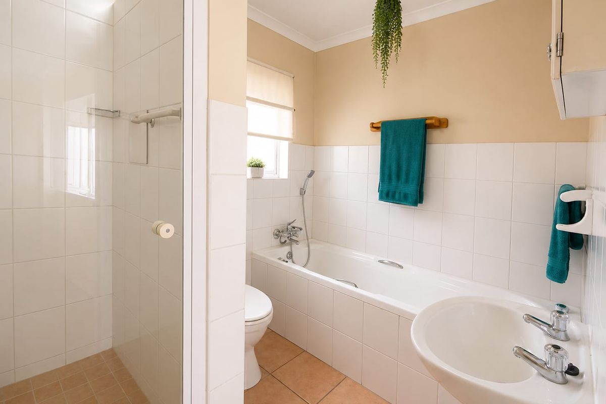 A functional bathroom featuring a separate shower enclosure, bathtub, pedestal basin, and toilet with neutral wall tiles and ceramic floor tiling.