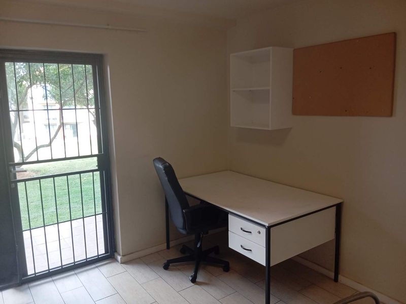 A functional home office space featuring tiled flooring and a secure exterior door with direct access to the garden area.