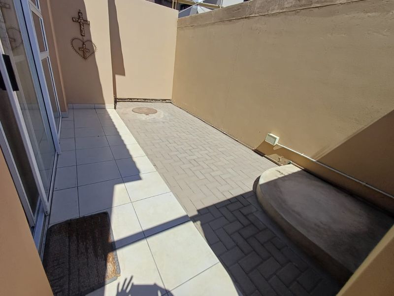 A compact, paved outdoor patio area featuring a sliding door entrance, boundary walls, and external electrical access, suitable for a small seating arrangement.