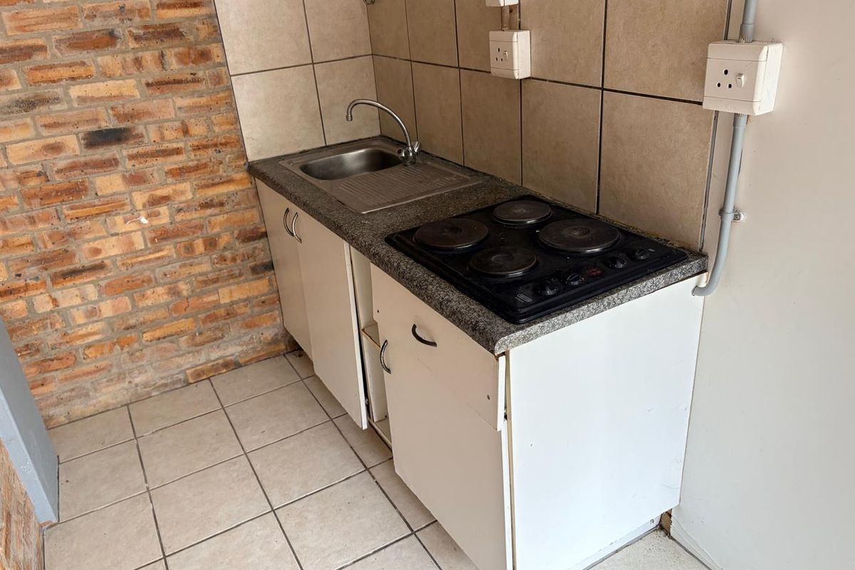 Compact kitchenette featuring a stainless steel sink, built-in electric hob, tiled splashback, and exposed brick wall detail.
