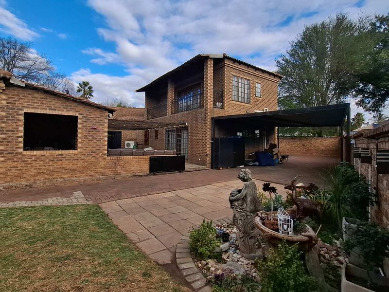 Rear view of a double-story face brick house featuring a paved courtyard, covered patio area, and a carport.