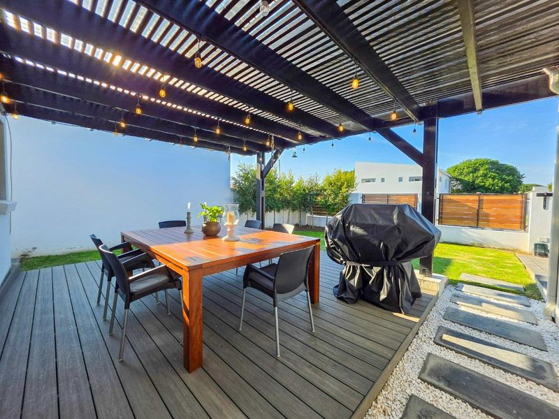 A well-maintained outdoor patio featuring timber decking, a covered pergola with string lighting, and a landscaped garden area.