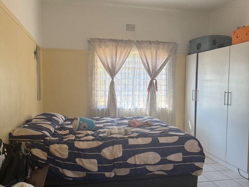 A functional bedroom featuring tiled flooring, a built-in wardrobe, and a window with security bars, offering a neutral base for potential updates.