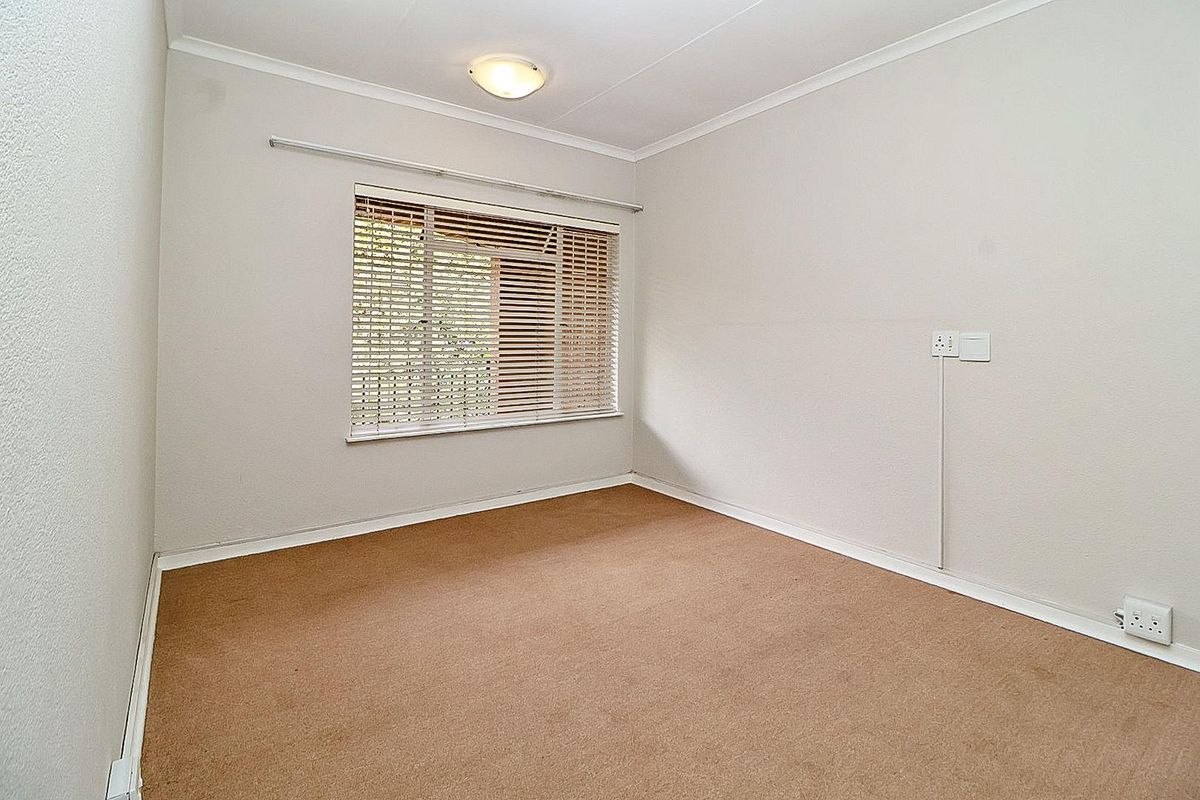 A neutral, empty bedroom featuring carpeted flooring, a window with fitted blinds, and standard electrical points.