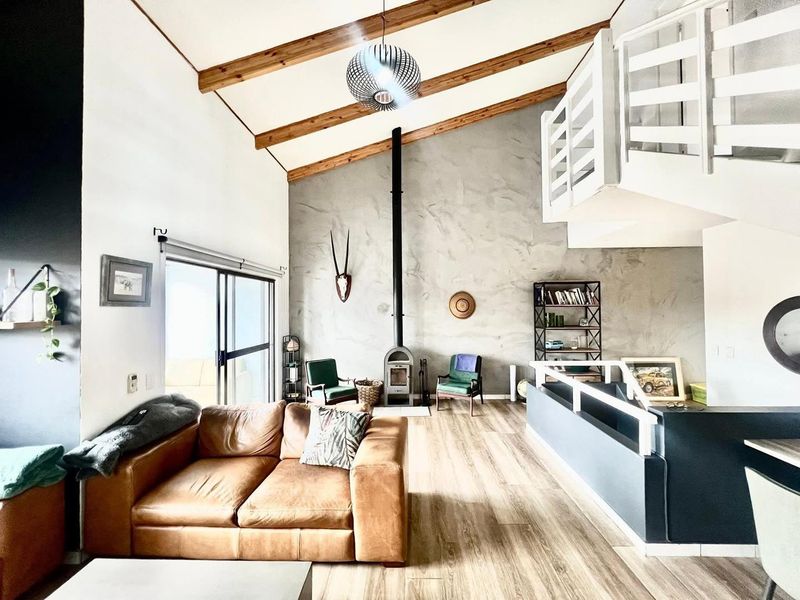 Spacious living area featuring a vaulted ceiling with exposed timber beams, a modern freestanding fireplace, and a mezzanine level overlooking the room.