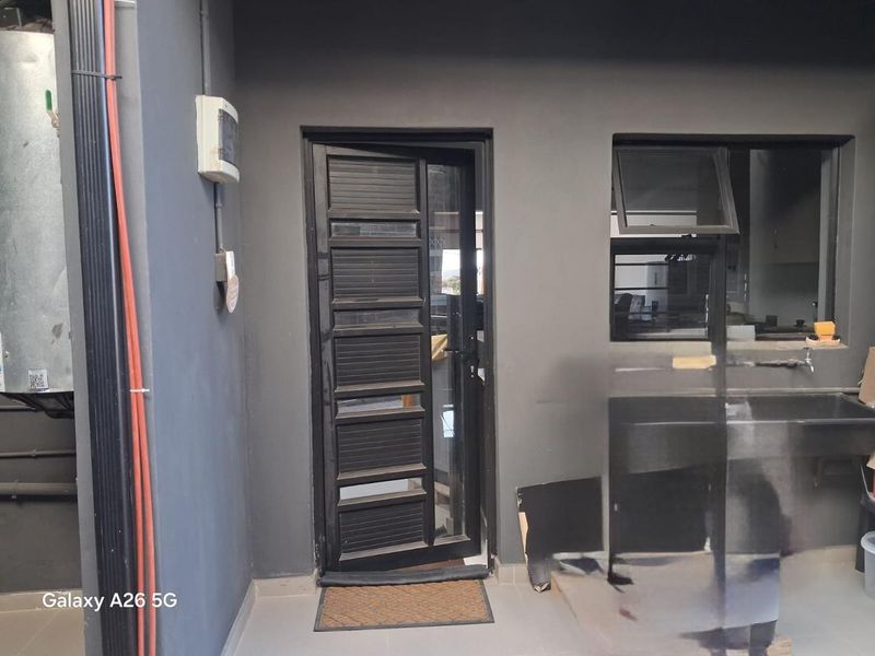 A functional scullery or utility area featuring a stainless steel sink, tiled flooring, and direct access to the exterior via a dark-framed door.