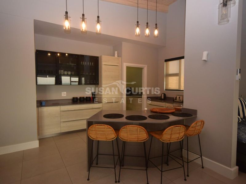 Modern kitchen featuring sleek built-in cabinetry, stone countertops, a functional breakfast bar, and contemporary pendant lighting in an open-plan layout.