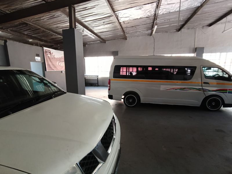 Spacious industrial garage area featuring exposed steel roof trusses, concrete flooring, and structural support columns, suitable for vehicle storage or workshop use.