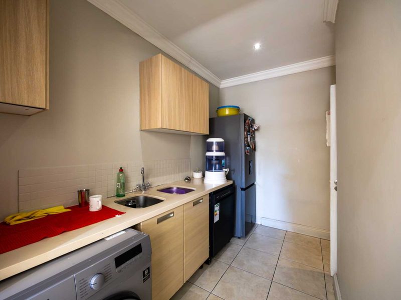 A functional scullery featuring built-in cabinetry, laminate countertops, a stainless steel sink, and tiled flooring, providing additional utility and storage space.