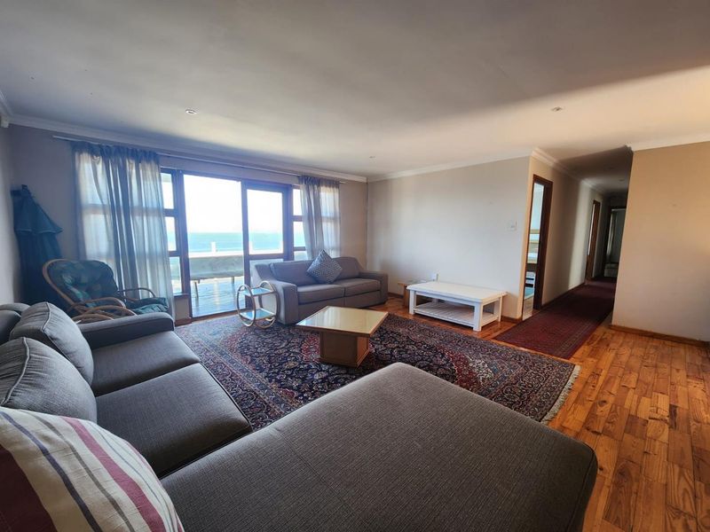 Spacious living room featuring hardwood flooring, recessed lighting, and large sliding glass doors that open to an outdoor deck with ocean views.