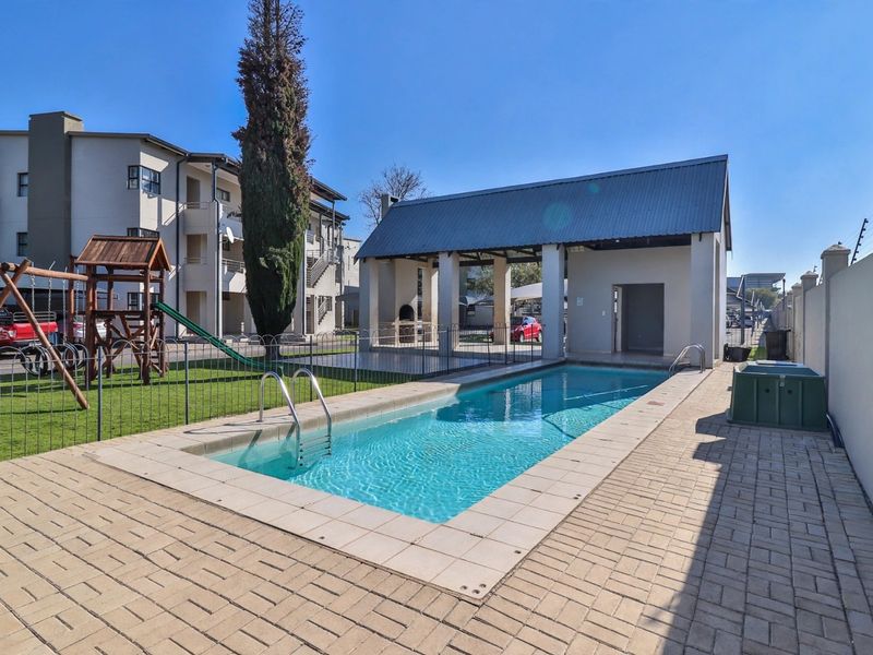 Communal pool area featuring a paved deck, covered patio with built-in braai, and secure perimeter walling within the townhouse complex.