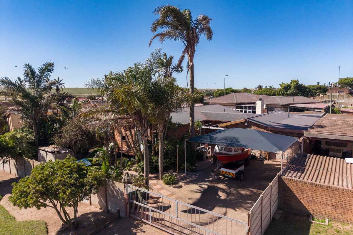Aerial view of the property featuring a paved driveway, secure perimeter wall with sliding gate, and a shade cloth carport.