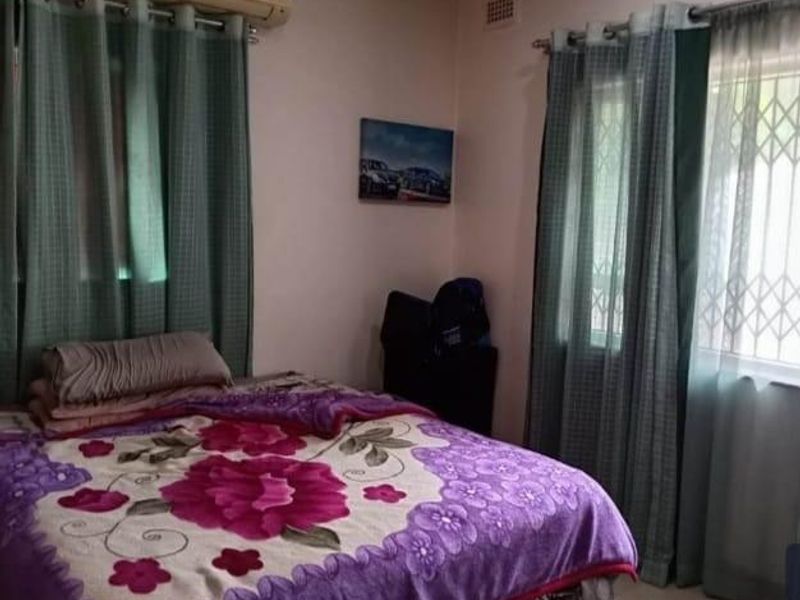 A functional bedroom featuring a wall-mounted air conditioning unit and windows fitted with security gates and curtain rods.