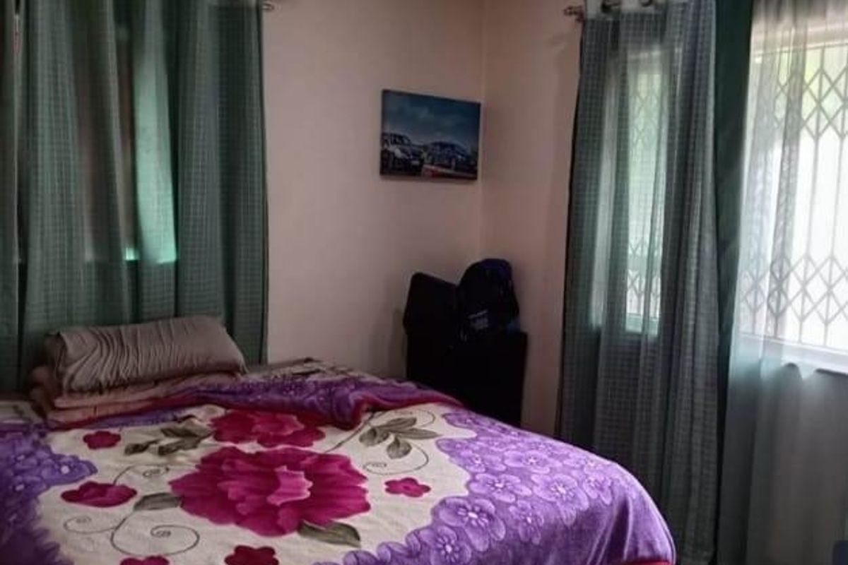 A functional bedroom featuring a wall-mounted air conditioning unit and windows fitted with security gates and curtain rods.