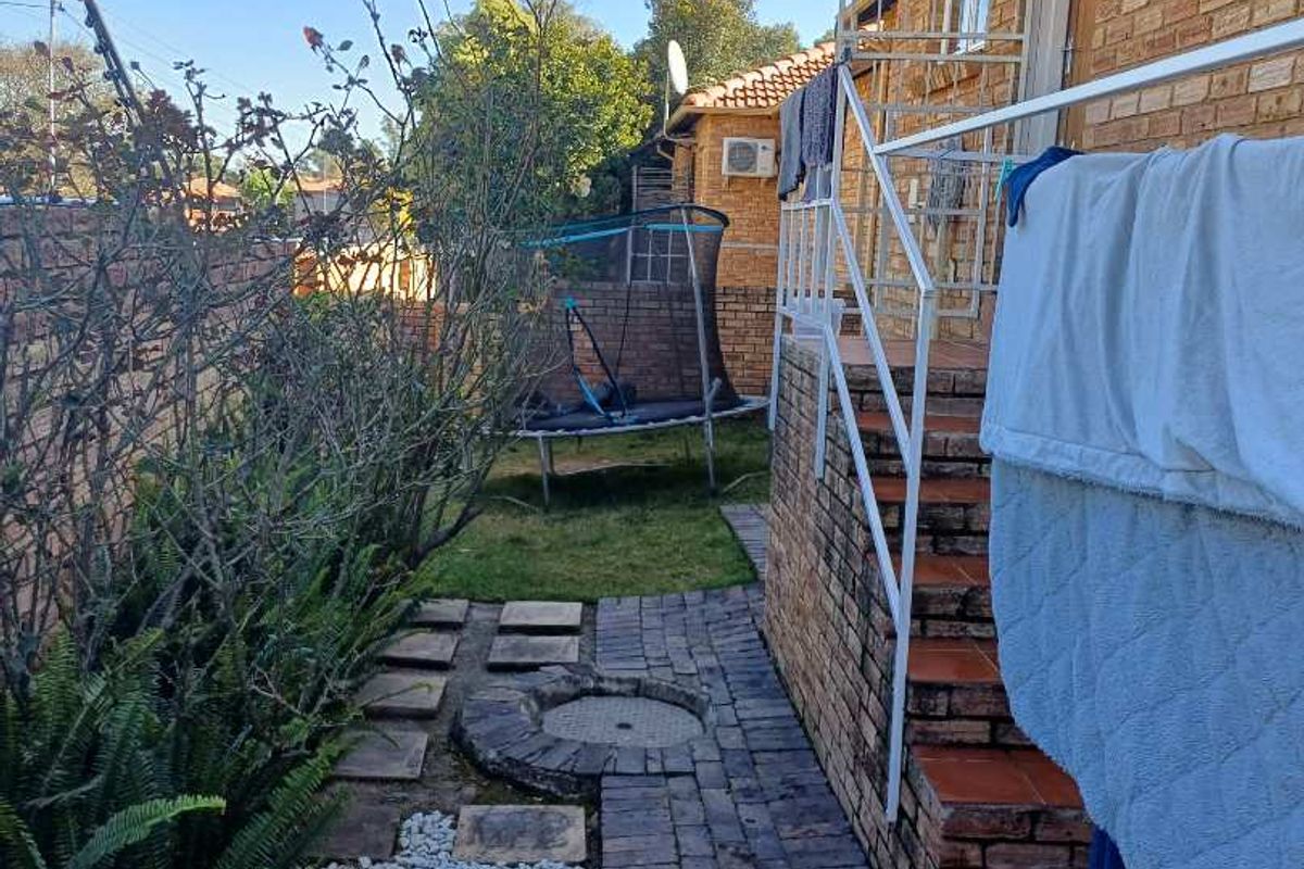 Rear exterior view of the property featuring a brick facade, paved walkway, and an external staircase leading to the entrance.
