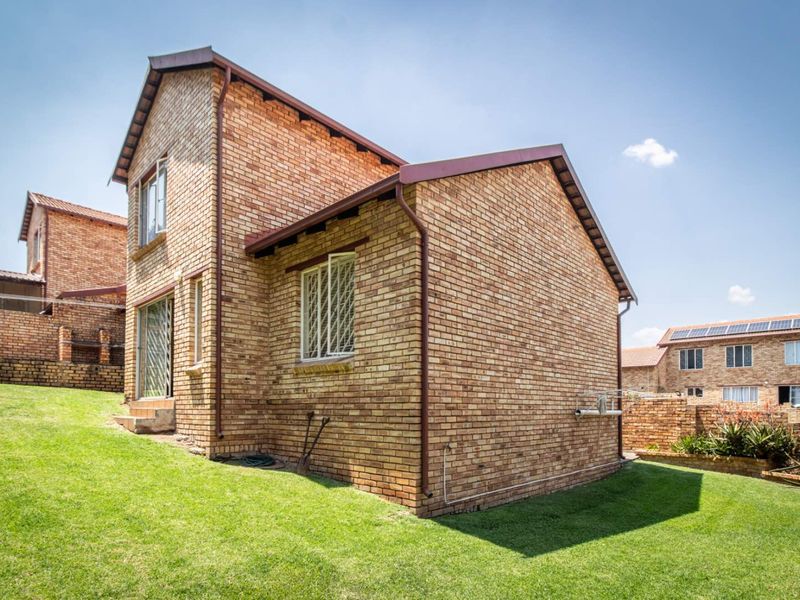 Rear view of a double-story face brick townhouse featuring a gabled roof, security bars on windows, and a well-maintained lawn area.