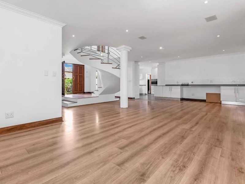 Spacious open-plan living area featuring modern laminate flooring, a striking spiral staircase, and a sleek kitchen with ample cabinetry and counter space.