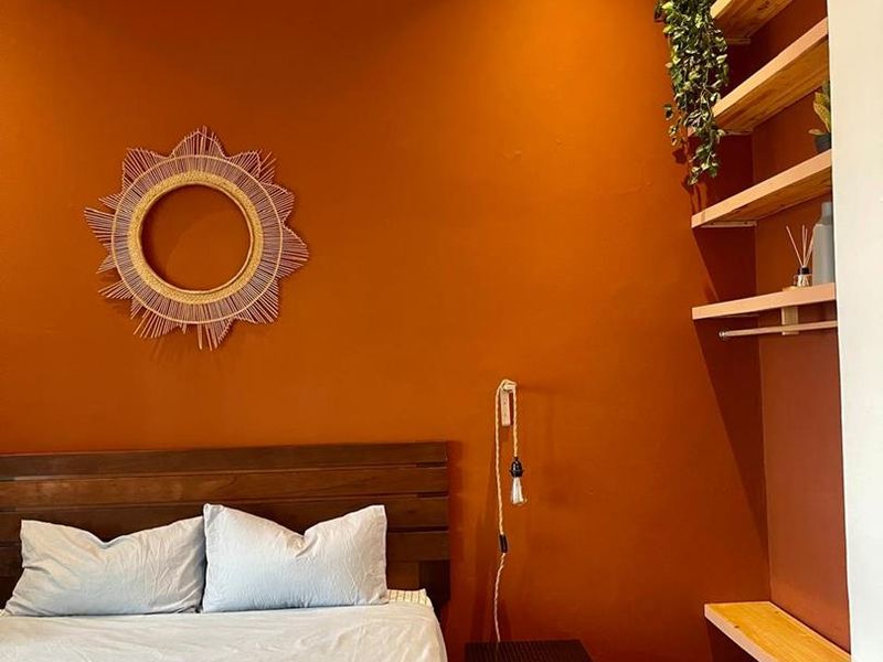 A cozy bedroom featuring a bold terracotta accent wall, built-in timber shelving, and recessed downlighting, creating a warm and inviting atmosphere.