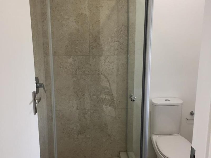 A clean, functional bathroom featuring a glass-enclosed shower with neutral stone-look wall tiles and a standard white toilet.