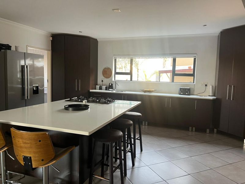 Modern kitchen featuring a large central island with a gas hob, stone countertops, ample dark cabinetry, and tiled flooring.