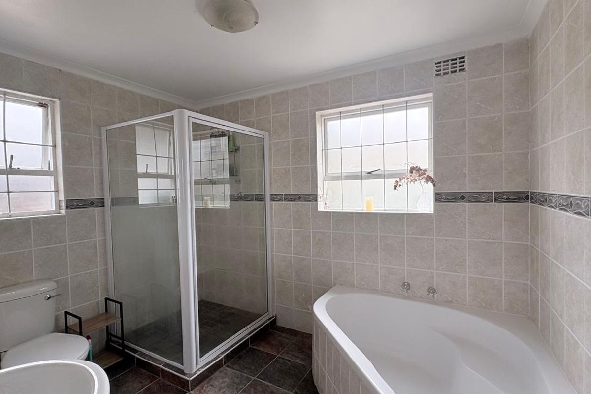 A functional bathroom featuring a corner bathtub, separate shower enclosure, and neutral wall tiling throughout.