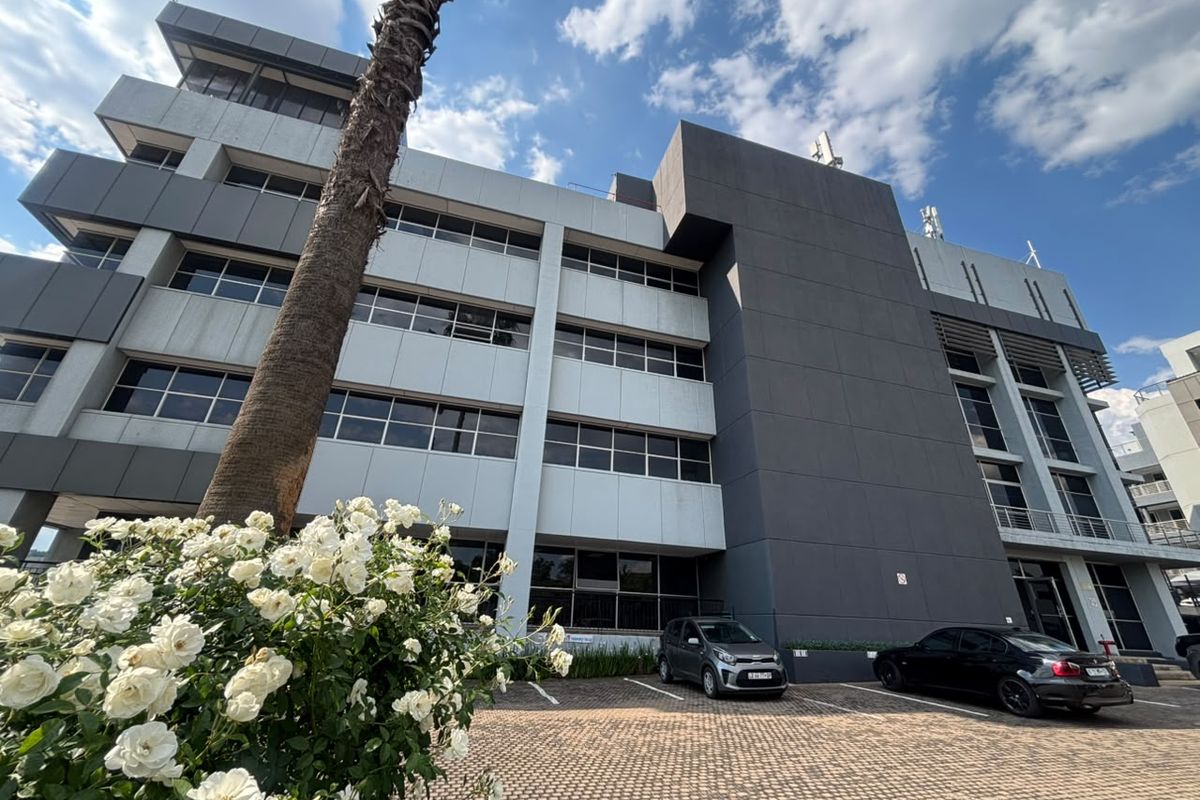 A modern multi-story office building featuring a contemporary facade with aluminum cladding and large windows, situated above a paved parking area.