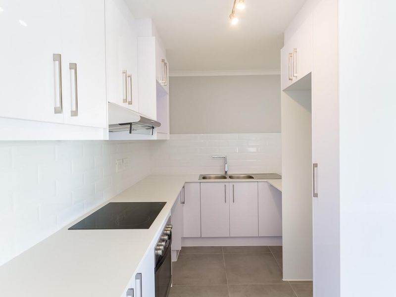 Modern, clean-lined kitchen featuring white cabinetry, subway tile backsplash, integrated electric hob and oven, and durable stone countertops with a double sink.
