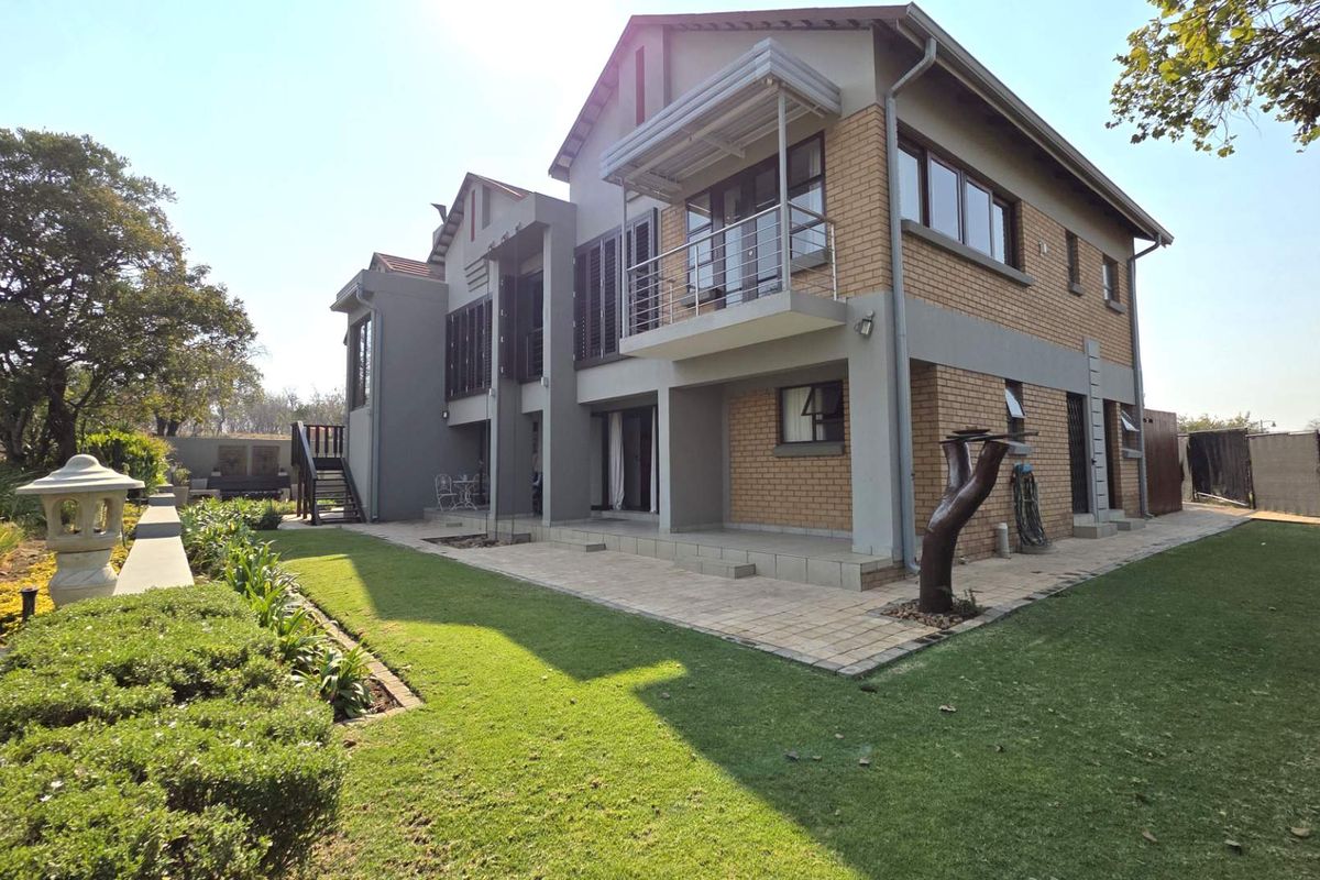 A well-maintained rear elevation of a two-story brick house featuring a paved patio, balcony, and landscaped garden area.