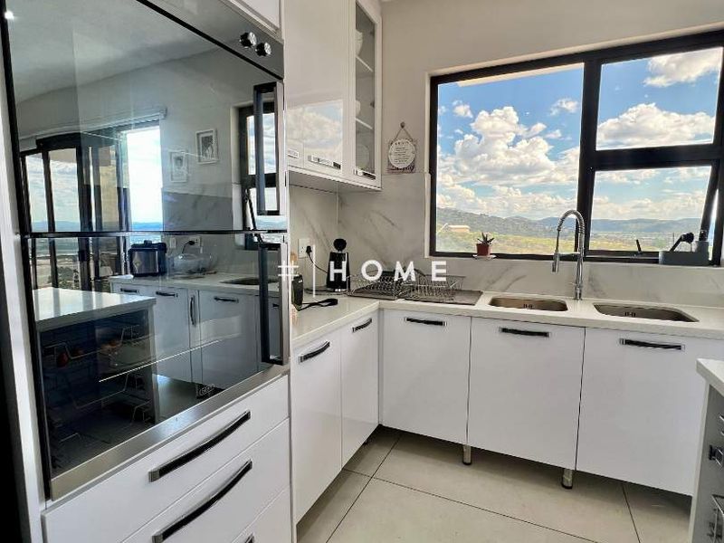 Modern kitchen featuring white cabinetry, stone countertops, built-in oven, and a double sink with scenic views through a large window.