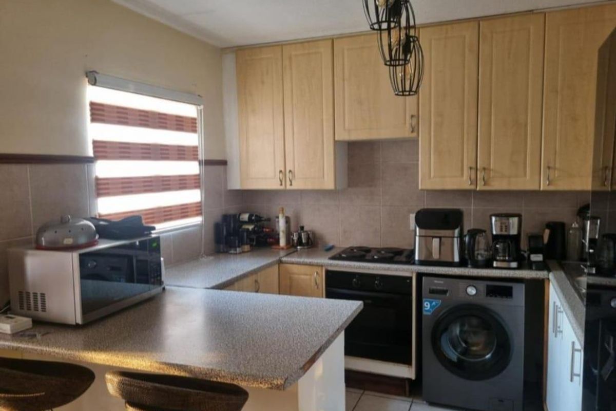 A functional kitchen featuring light wood-finish cabinetry, laminate countertops, a breakfast nook, and integrated cooking appliances with tiled flooring and backsplash.