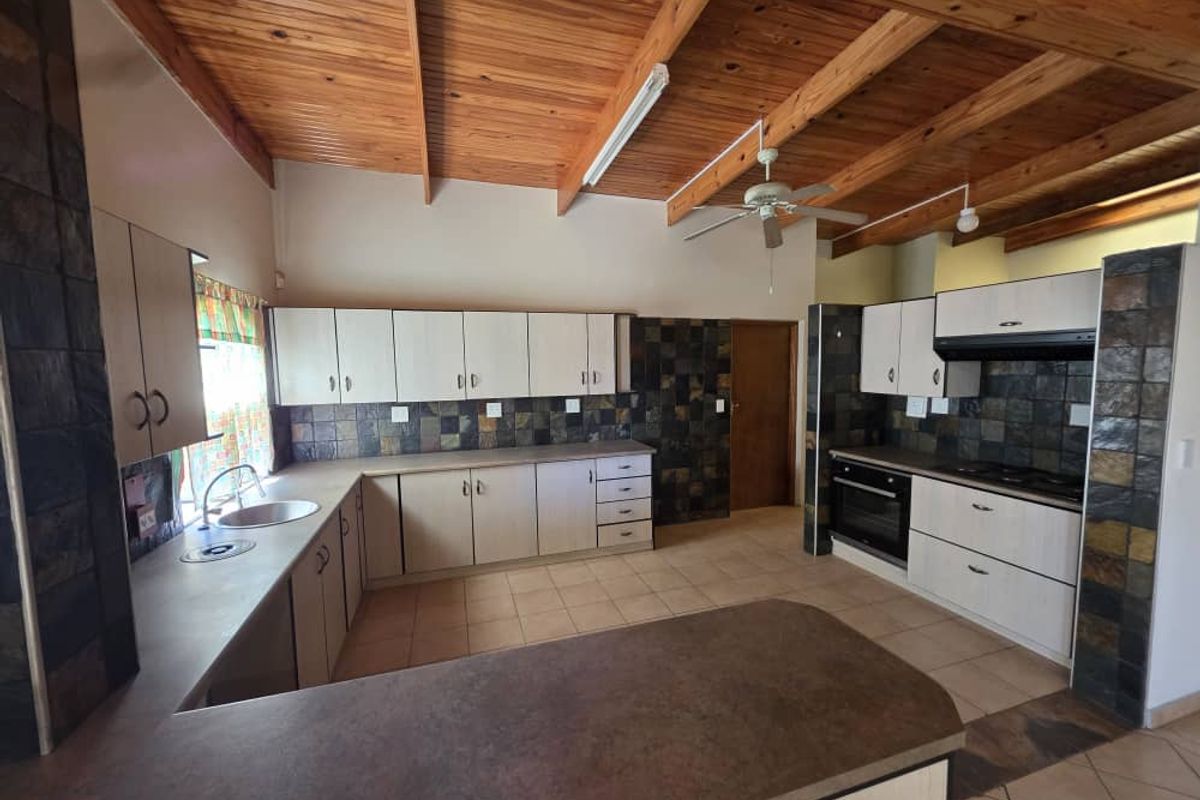 Spacious kitchen featuring light-toned cabinetry, dark stone-style tile splashbacks, a built-in oven, and a distinctive exposed timber beam ceiling.