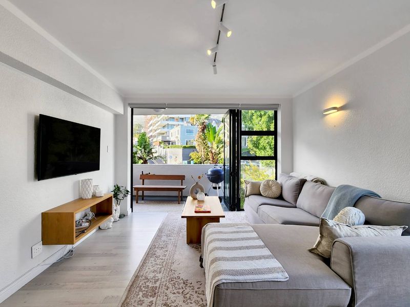 Bright living room featuring modern track lighting, laminate flooring, and seamless access to an outdoor balcony through large bi-fold glass doors.