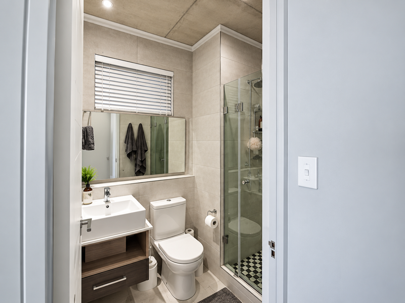 Modern bathroom featuring a vanity with basin, toilet, and a glass-enclosed shower with contemporary tiled finishes and neutral tones.