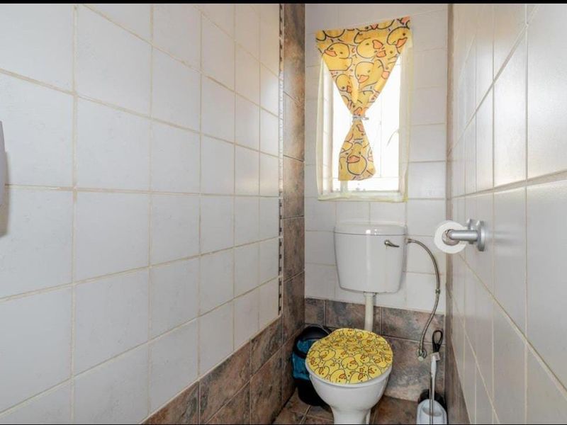 A compact guest bathroom featuring tiled walls and flooring, equipped with a standard toilet and a small window for natural light.