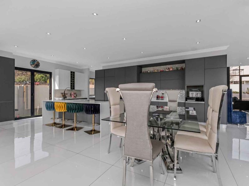 Modern open-plan kitchen and dining area featuring sleek dark cabinetry, a central island, and polished tile flooring with abundant natural light.
