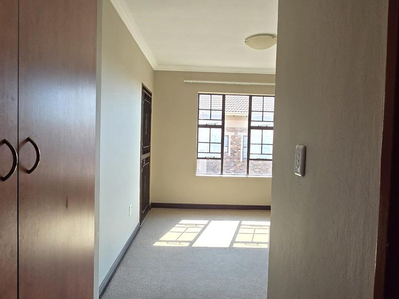 An empty bedroom featuring built-in cupboards, carpeted flooring, and a window with security bars, viewed from the doorway.