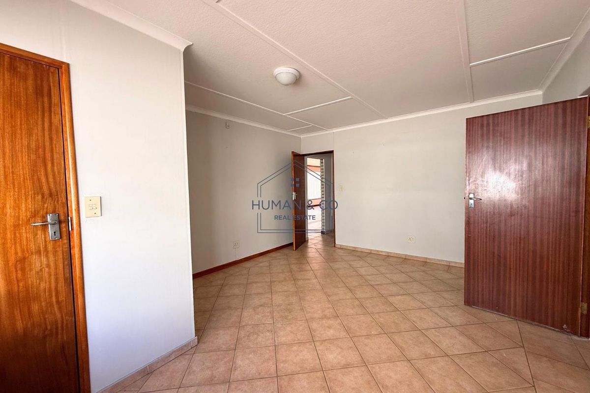 A vacant, neutrally painted room featuring tiled flooring, wooden doors, and a simple ceiling finish, suitable for use as a bedroom or office space.