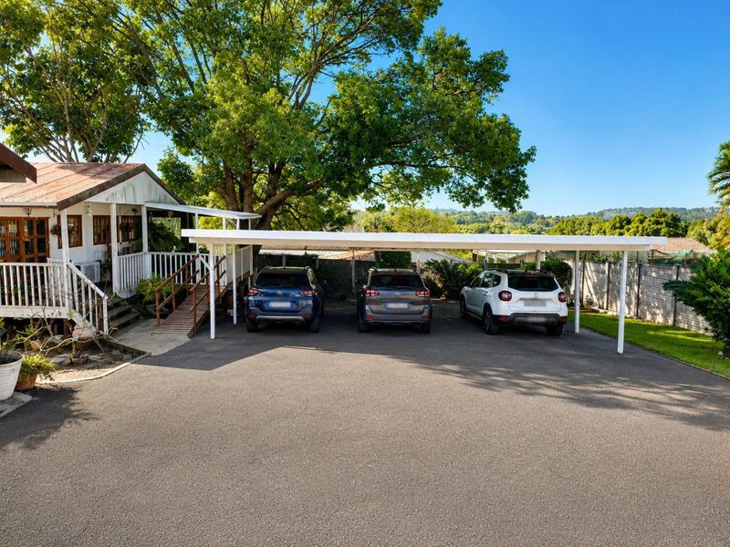 Front exterior view featuring a spacious asphalt driveway, a large triple carport, and a raised timber deck entrance to the main house.