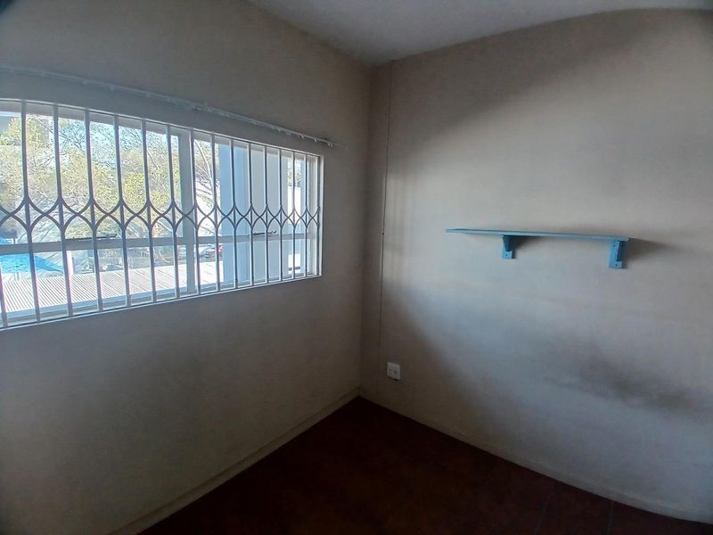 An empty bedroom featuring tiled flooring, a wall-mounted shelf, and a window fitted with security bars.