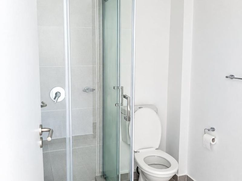 A clean, modern bathroom featuring a glass-enclosed shower with grey tiling and a standard white toilet.