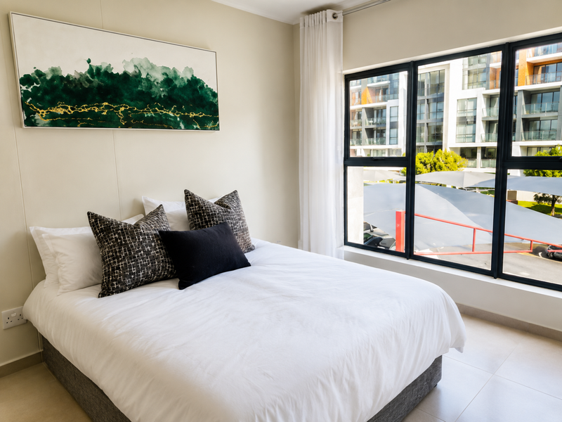 A bright and modern bedroom featuring large windows with natural light, neutral wall tones, and tiled flooring.