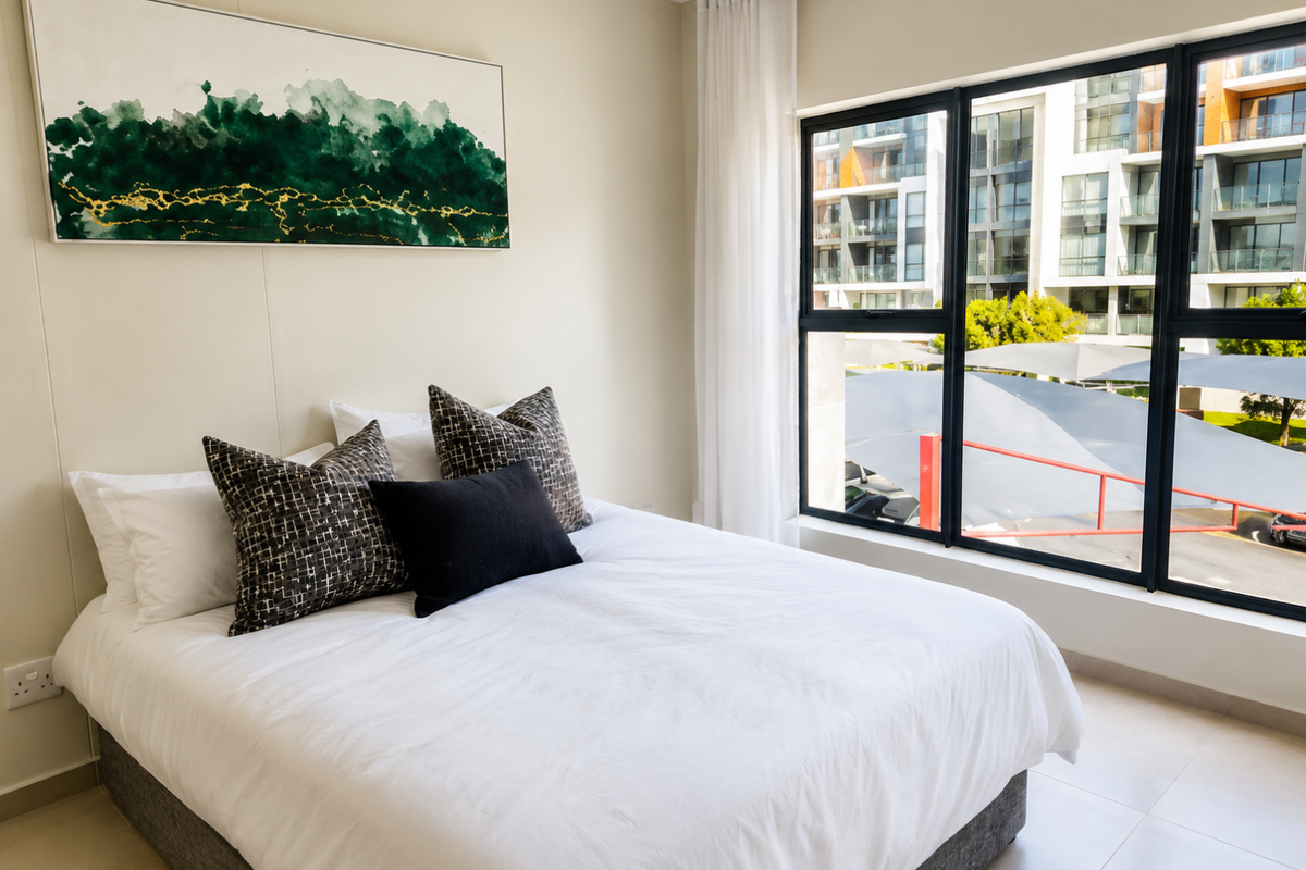 A bright and modern bedroom featuring large windows with natural light, neutral wall tones, and tiled flooring.