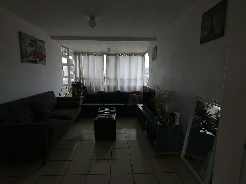 A living room area featuring tiled flooring and a large window, providing natural light to the space.